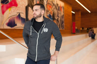 A woman wearing a dark gray zip-up hooded sweatshirt with drawstrings and the white HashiCorp H icon on her left chest. 